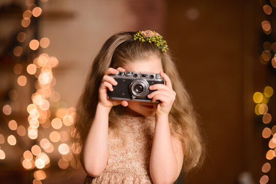  little girl in a festive dress with flowing hair takes pictures on a vintage camera.