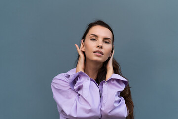 Pretty stylish woman in purple shirt posing on blue wall background, long dark beautiful hair, natural makeup, soft skin