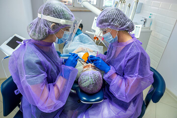 Beautiful girl in a patient's bib and orange UV goggles in a dental clinic.