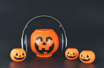  big plastic halloween pumpkin  coverd with headphones, isolated on black  background with smaller pumpkins,  copy space. Halloween music or podcast.