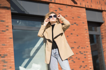 Portrait of a young Caucasian girl in a coat and sunglasses in the city on an autumn day.
