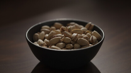 roasted pistachios in black bowl on walnut table