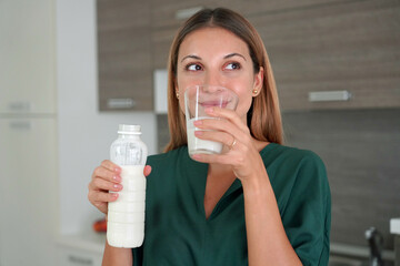 Portrait of young smiling woman drinking kefir. Beautiful girl holds a glass of milk in the morning.