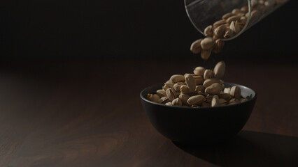 roasted pistachios falling into black bowl on walnut table