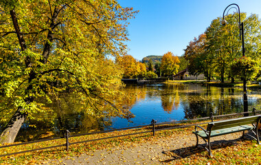City park and lake with colorful fall trees leaf mosaic in historic old town quarter of Andrychow with Beskidy Mountains in background in Lesser Poland
