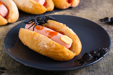 An amputated sausage finger in ketchup in a bun on a plate. Halloween recipe.