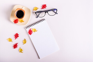 Autumn still life notebook, coffee cup, glasses and colored leaves on a pink background. Top view.