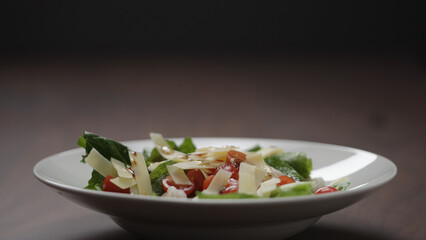 making salad pour dressing over in white bowl