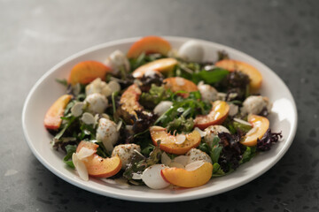 Closeup salad with nectarines, mozzarella and mixed greens in white plate on concrete background