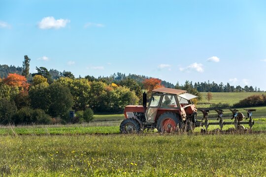 Old red Tractor Plowing in Autumn, Farmer plowing stubble field in tractor preparing plows the land. Agricultural works at farmlands in Czech Republic.