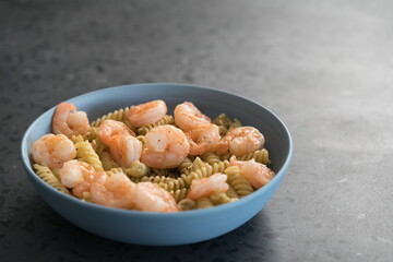 Fusilli with shrimps and pesto in a blue bowl on concrete background