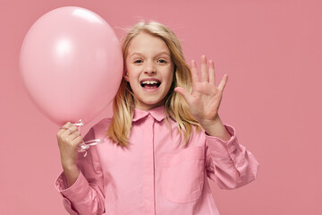 happy, beautiful girl of school age, blonde, stands in a pink shirt with an inflatable pink ball in her hand and smiles broadly, showing five fingers at the camera
