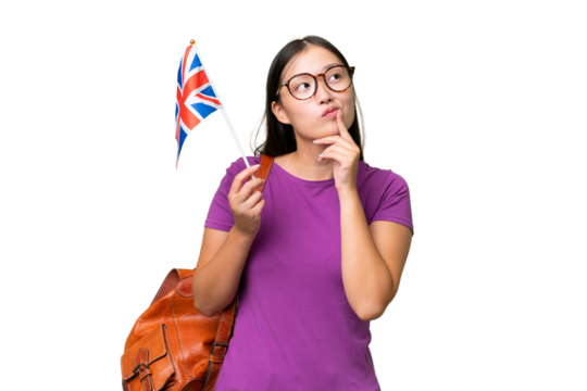 Young Asian woman holding an United Kingdom flag over isolated background having doubts while looking up