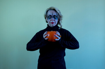 A woman in black clothes holds an orange pumpkin in her hands. Halloween woman portrait. Cold toning