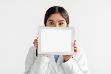 Young hindu lady doctor in coat show tablet with blank screen, isolated on white background