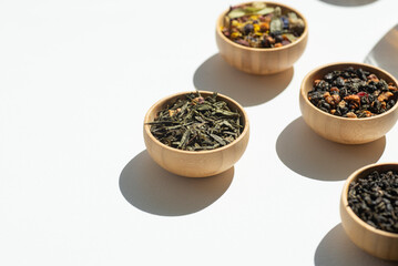 Different types of green, black and herbal tea in a wooden bowl. Variety of dry leaves and flowers. Organic high-quality ingredients for a drink. Soft focus on one bowl - obrazy, fototapety, plakaty