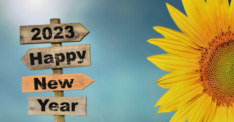2023 happy new year written on a direction sign with petals of sun flower on blue sky © coco