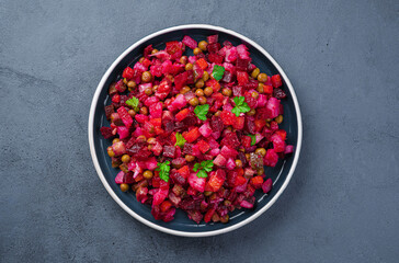Vegetable salad with beetroot, pickled cucumbers, peas and fresh herbs on a dark background. Traditional vinaigrette. Close-up, top view