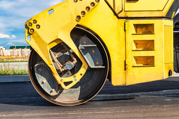 Vibratory road roller lays asphalt on a new road under construction. Close-up of the work of road machinery. Construction work on the construction of urban highways. - obrazy, fototapety, plakaty