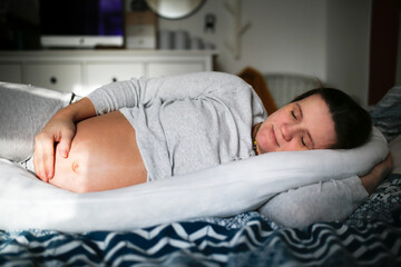 Middle-aged pregnant woman sleeps on special pillow for pregnant women in bedroom.