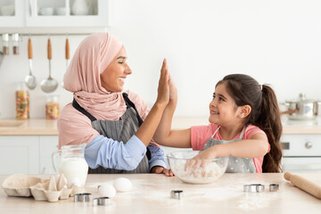 Obraz na płótnie Canvas Happy Muslim Mom And Daughter Giving High Five While Baking In Kitchen