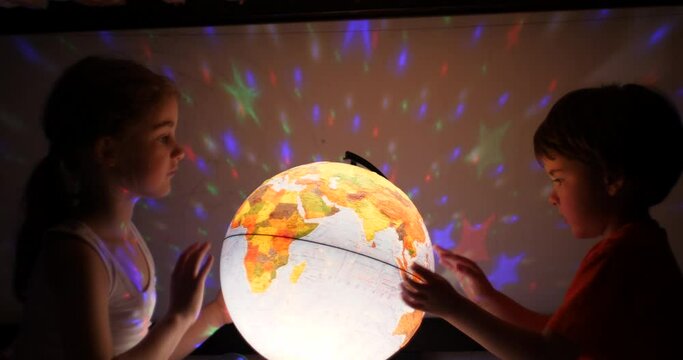 Kids Playing With Globe at Night. Children Sits on Bed in Evening Light Dreaming Vacation. Children Looking at Illuminated Globe, Exploring World, Learning. Dreaming About Future Save of Our Planet.