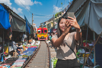Obraz na płótnie Canvas Asian traveler with mobile phone travel at Mae Klong railway market in Thailand