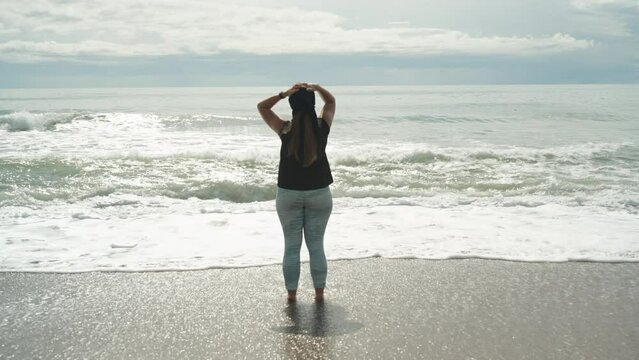 Stormy sea and clouds, a plump girl is standing on the beach and holding her head with her hands, The waves are hitting my legs.