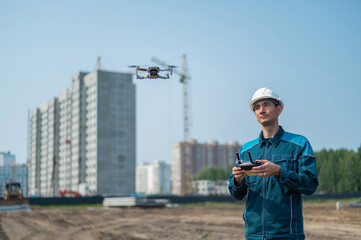 A man in a helmet and overalls controls a drone at a construction site. The builder carries out...