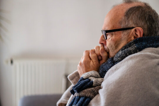Senior man wrapped in blanket feeling cold at home