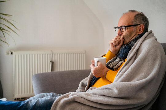 Man holding mug feeling cold sitting on sofa at home