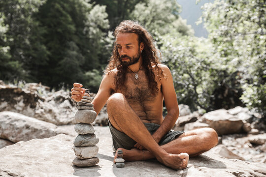 Shirtless young hipster stacking stones on rock