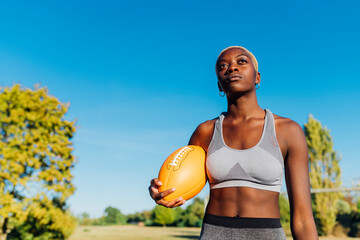 Contemplative sportswoman with American football on sunny day