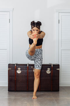 Woman exercising on one leg by treasure chest in front of white wall