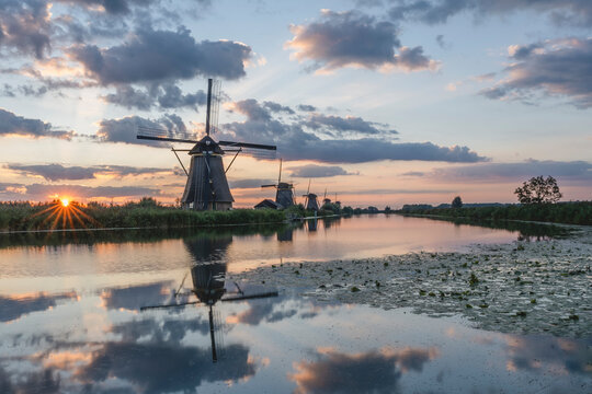 Netherlands, South Holland, Kinderdijk, Countryside river and historic windmills at sunset