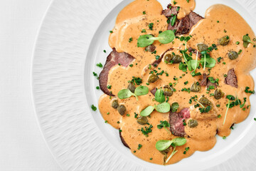 Vitello tonnato from veal with sauce in a white plate on a white background. Close-up, selective focus.