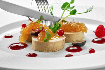 Foie gras with apple confit and berry sauce in a white plate on a white background. Close-up,...