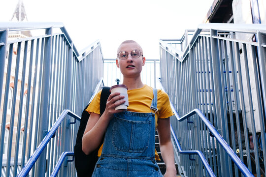 Thoughtful transgender person with disposable coffee cup on staircase - Powered by Adobe
