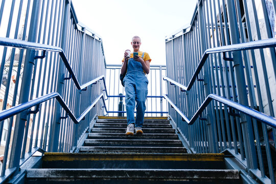 Non-binary person with disposable coffee cup using smart phone on steps