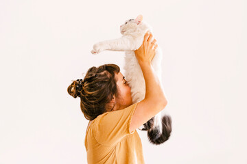 Woman holding aloft cat in front of wall at home
