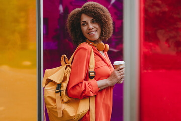 Smiling woman with backpack and disposable coffee cup by vibrant color glasses