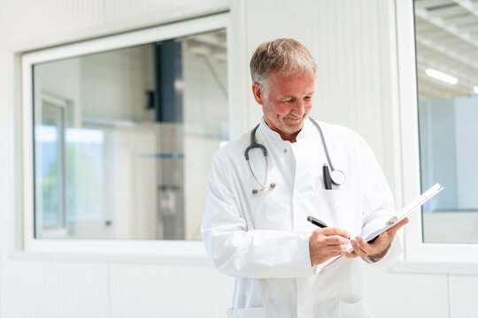 Smiling doctor writing on document at clinic