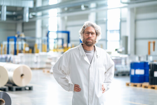 Man wearing lab coat standing with hands on hip in industry