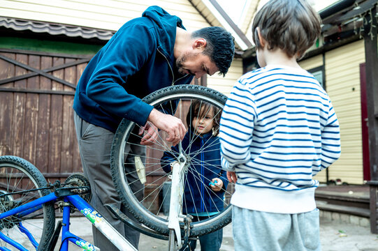 Man repairing wheel of bicycle by sons outside house