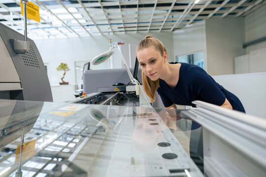 Young businesswoman examining 3D printing machine in industry