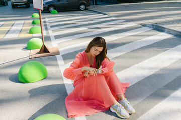 Woman checking time in watch sitting on road
