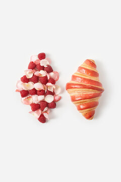 Fresh croissant by raspberries and rose petals shaped as similar over white background