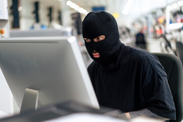 Computer hacker wearing mask using desktop PC at warehouse