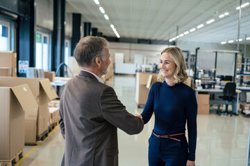 Happy businesswoman handshaking with colleague at warehouse