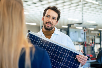 Engineer holding solar panel discussing with colleague
